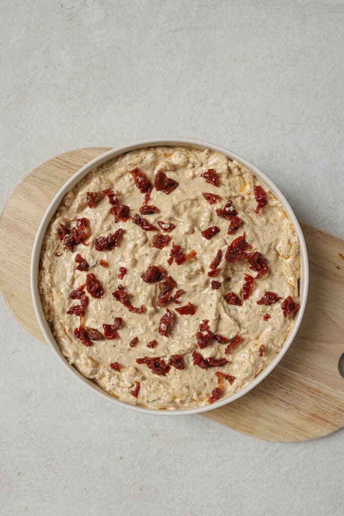 Adding sun dried tomatoes to the top of unbaked marry me chicken dip.