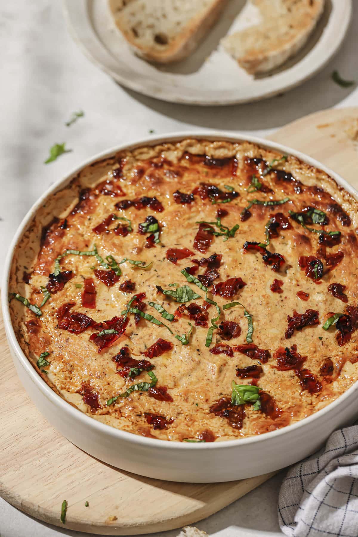 A dish of marry me chicken dip with a plate of crusty bread in the background.