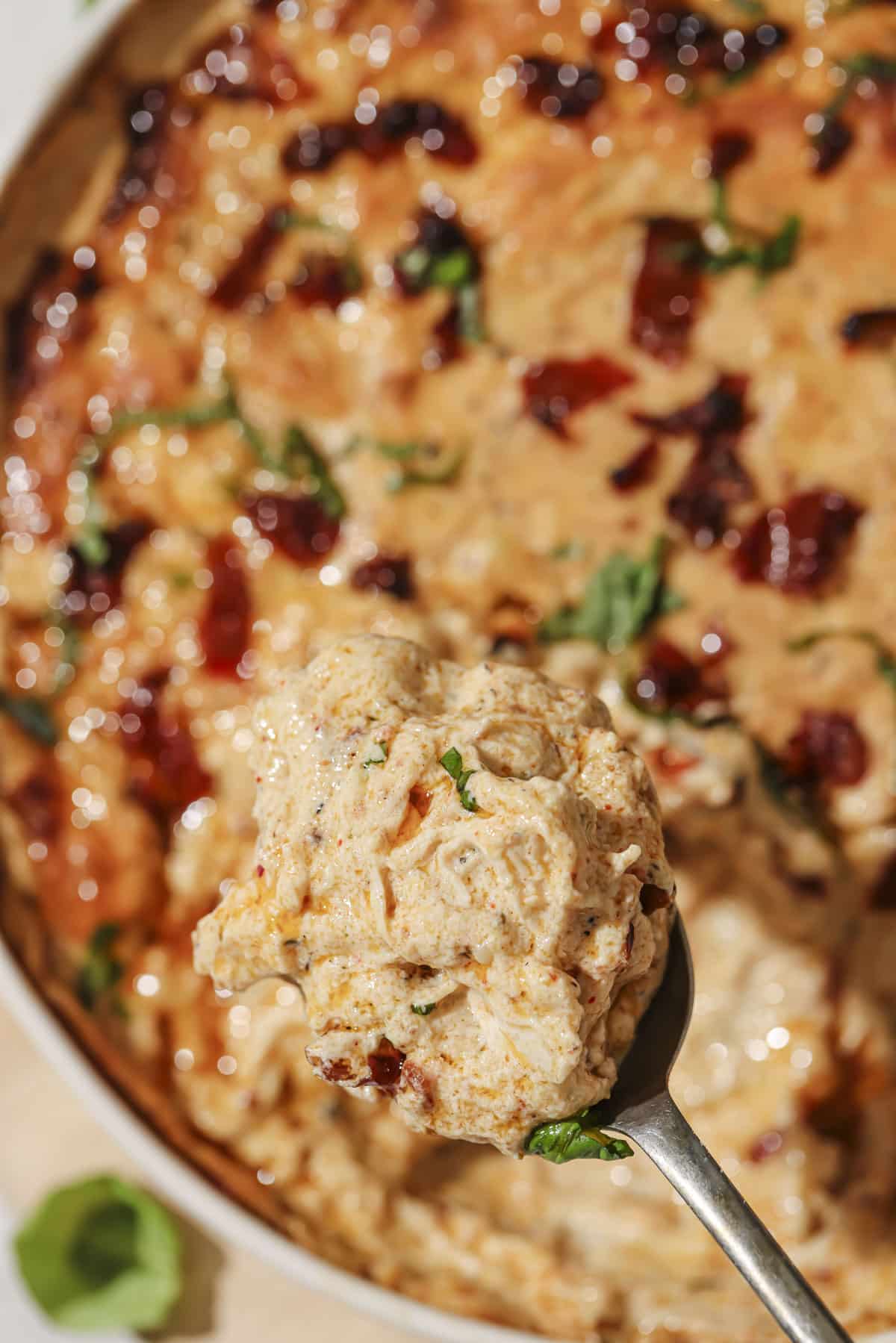 Using a spoon to get a big scoop of marry me chicken dip from a dish.