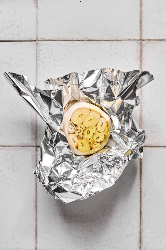 A head of garlic drizzled with olive oil and wrapped in aluminum foil.