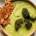 A bowl of soup with Parmesan crisps and roasted broccoli for garnish.