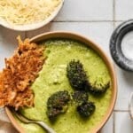 A bowl of soup on a counter with a bowl of Parmesan cheese to the side.