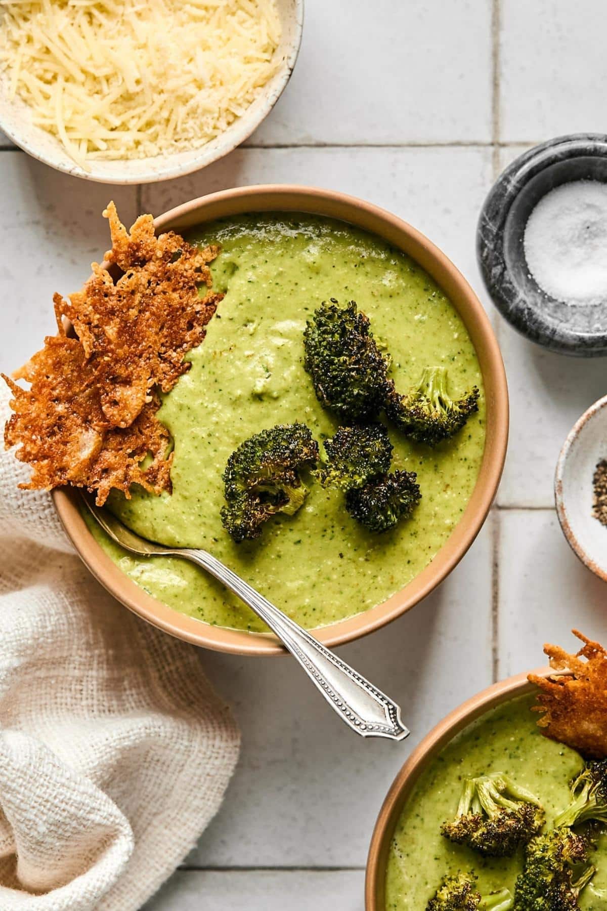 A bowl of broccoli feta soup on a countertop surrounded by ingredients.