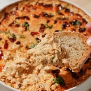 A hand scooping up marry me chicken dip with a piece of toasted bread.