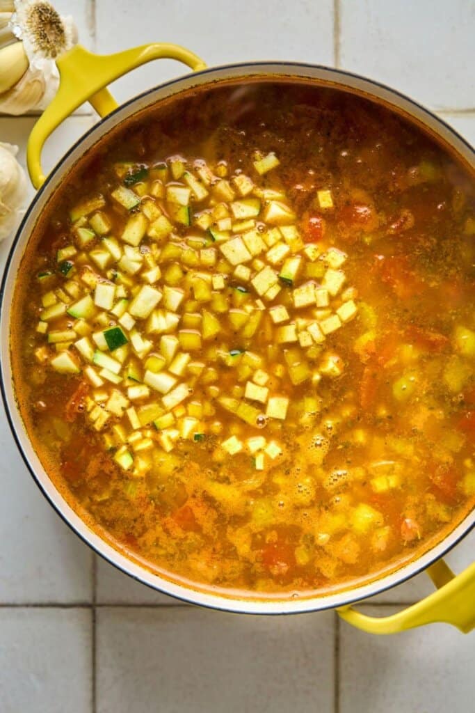 Adding chopped veggies to a soup pot filled with broth.