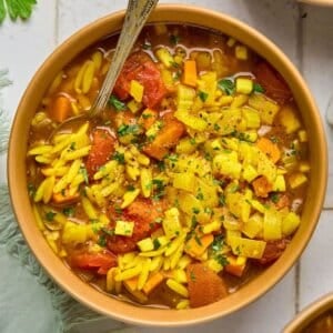 A bowl of vegetable orzo soup garnished with fresh herbs.