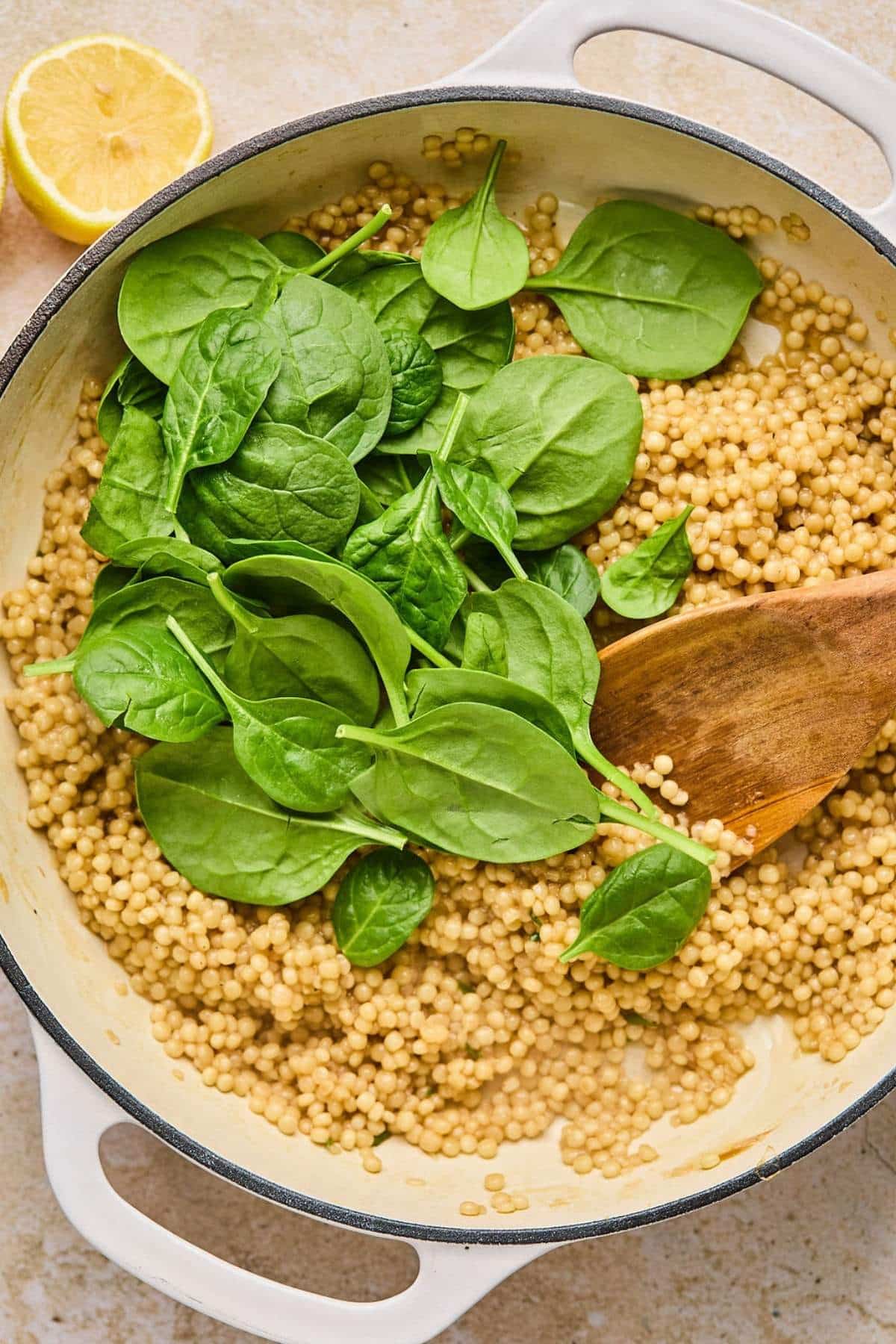 Mixing spinach with cooked couscous in a pot.