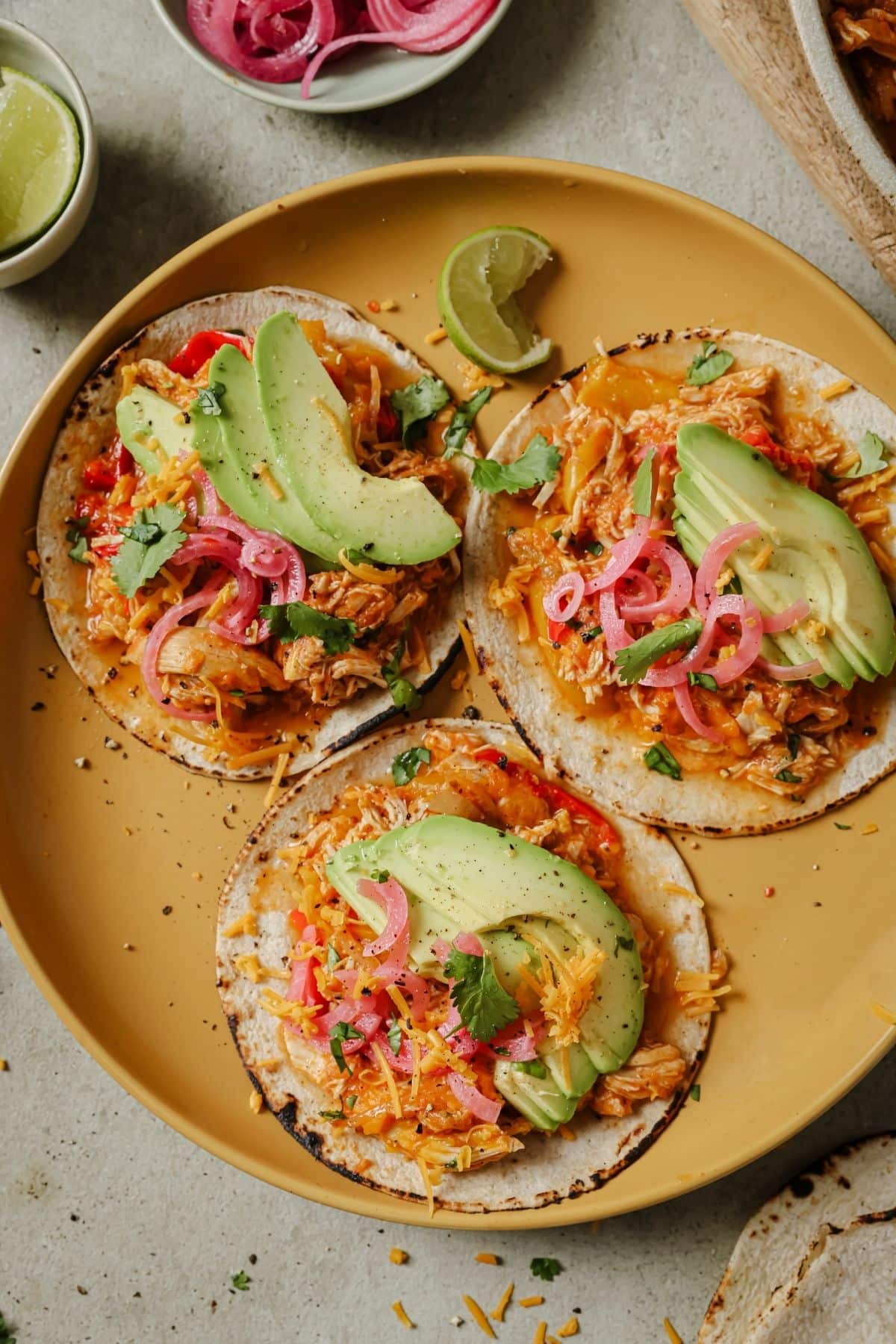 Slow cooker enchiladas served on tortillas and topped with avocado.