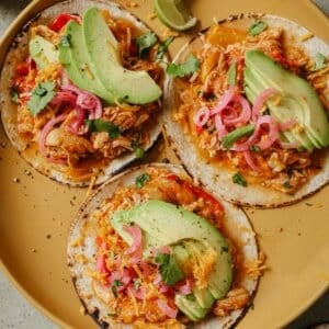 Plated slow cooker enchiladas on tortillas with toppings.