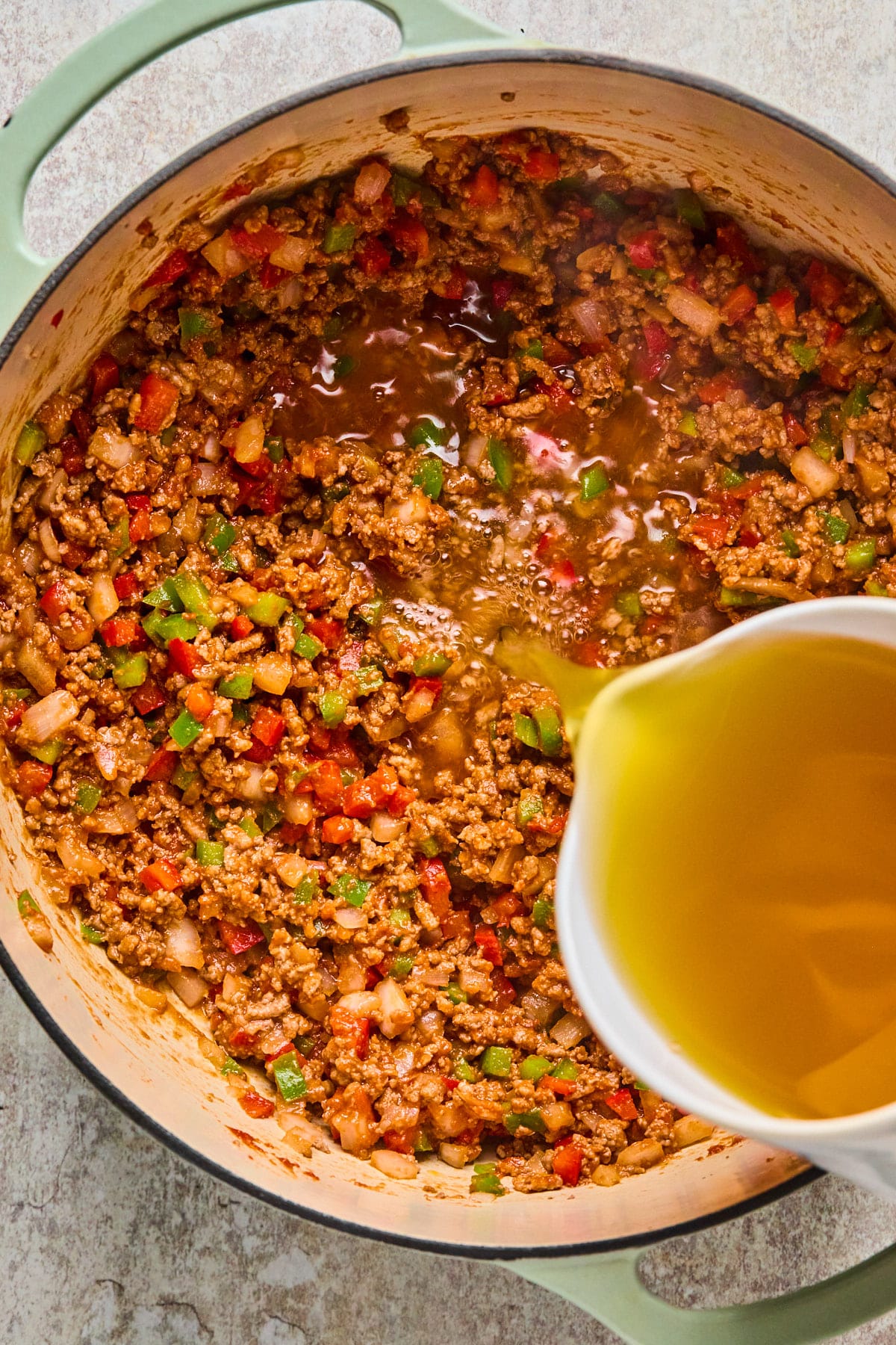 Vegetable broth being poured into a pot with beef and veggies.