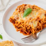 A slice of air fryer baked spaghetti on a white plate with a fork.