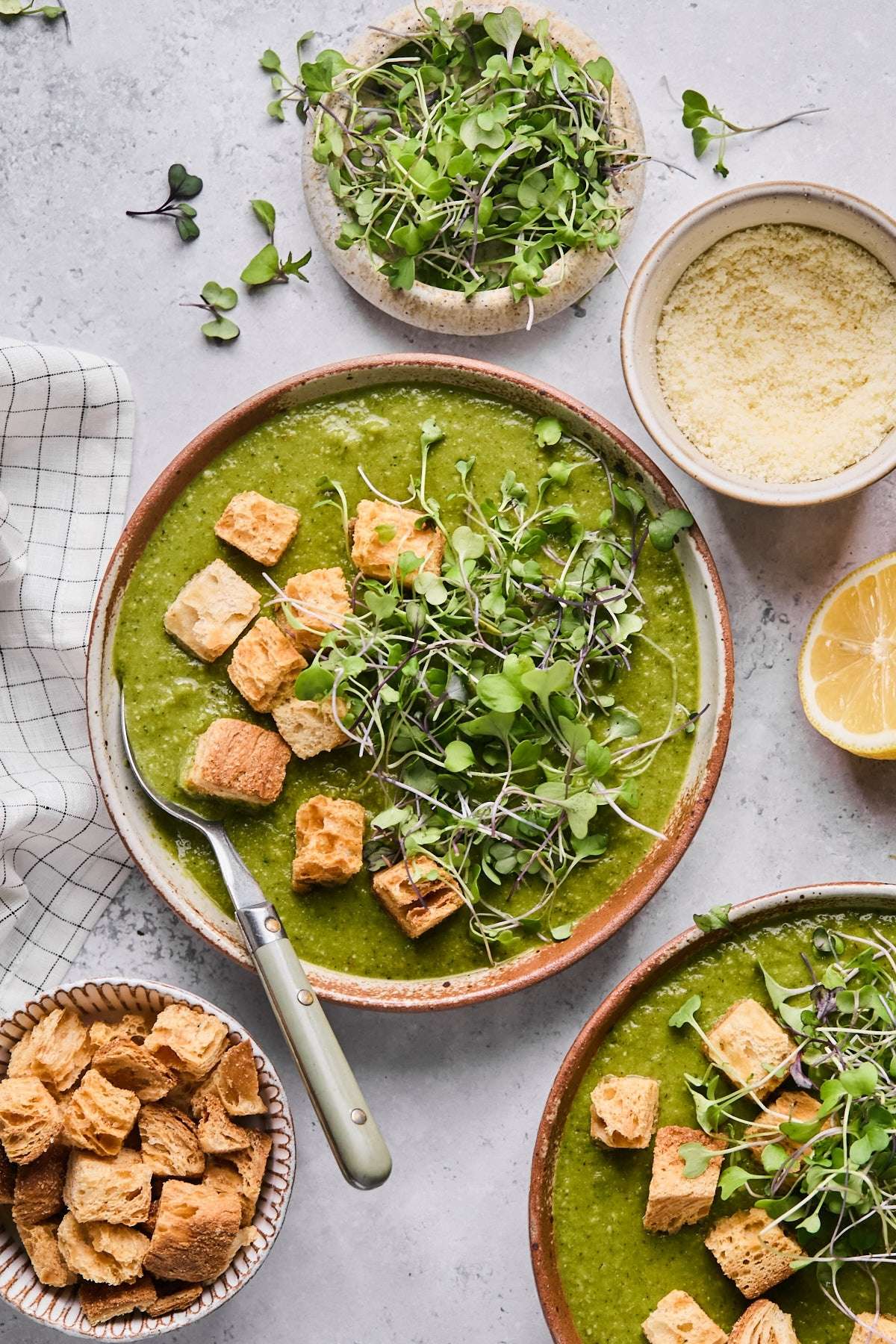 Green soup in a brown bowl with herbs, greens, and croutons on top.