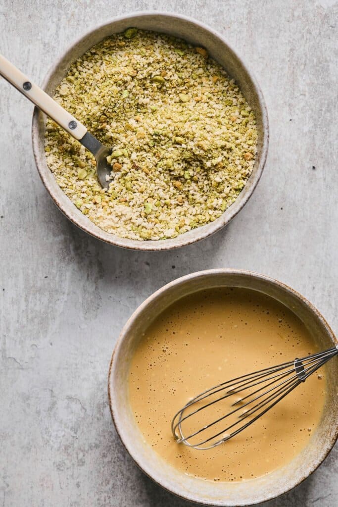 Two bowls, one with wasabi breadcrumbs and another with beaten egg.