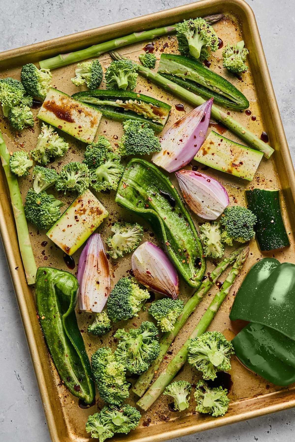 Vegetables for green soup on a baking sheet after being seasoned.