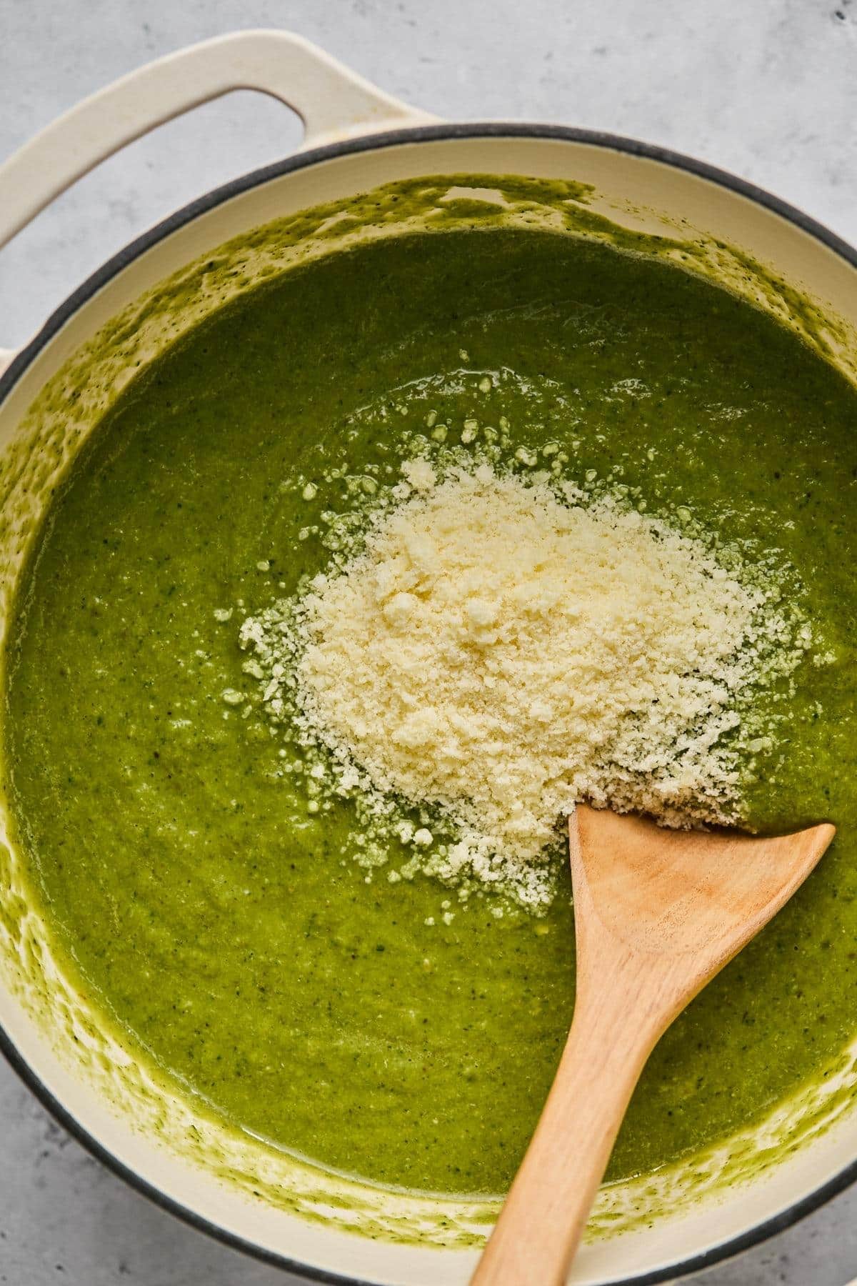 Parmesan cheese added to the Dutch oven with the green soup before being stirred with a wooden spoon.