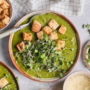 Finished Green Vegetable soup in a brown bowl with croutons and microgreens on top.