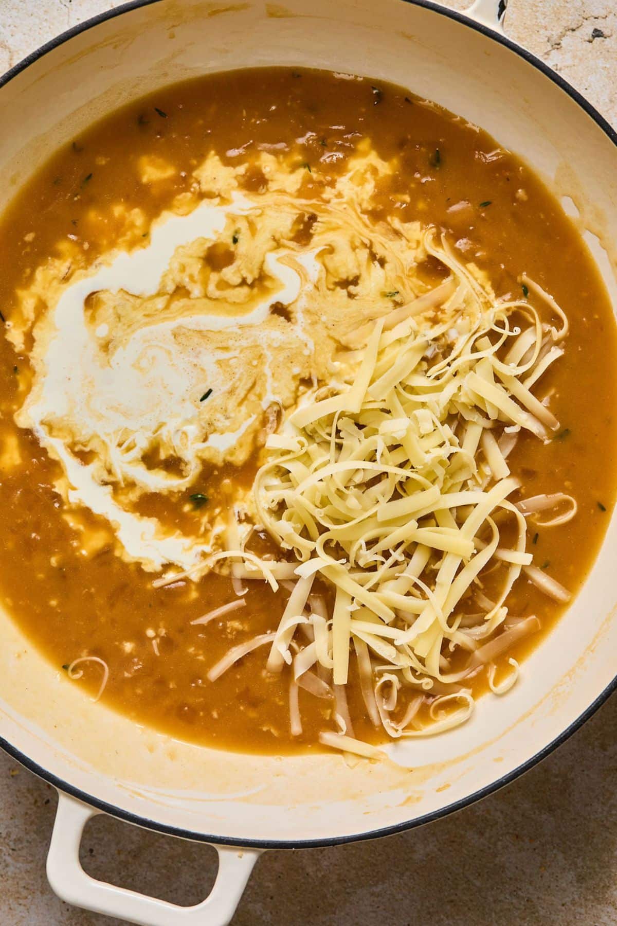 Cream and shredded cheese added to the skillet of French onion pasta sauce.