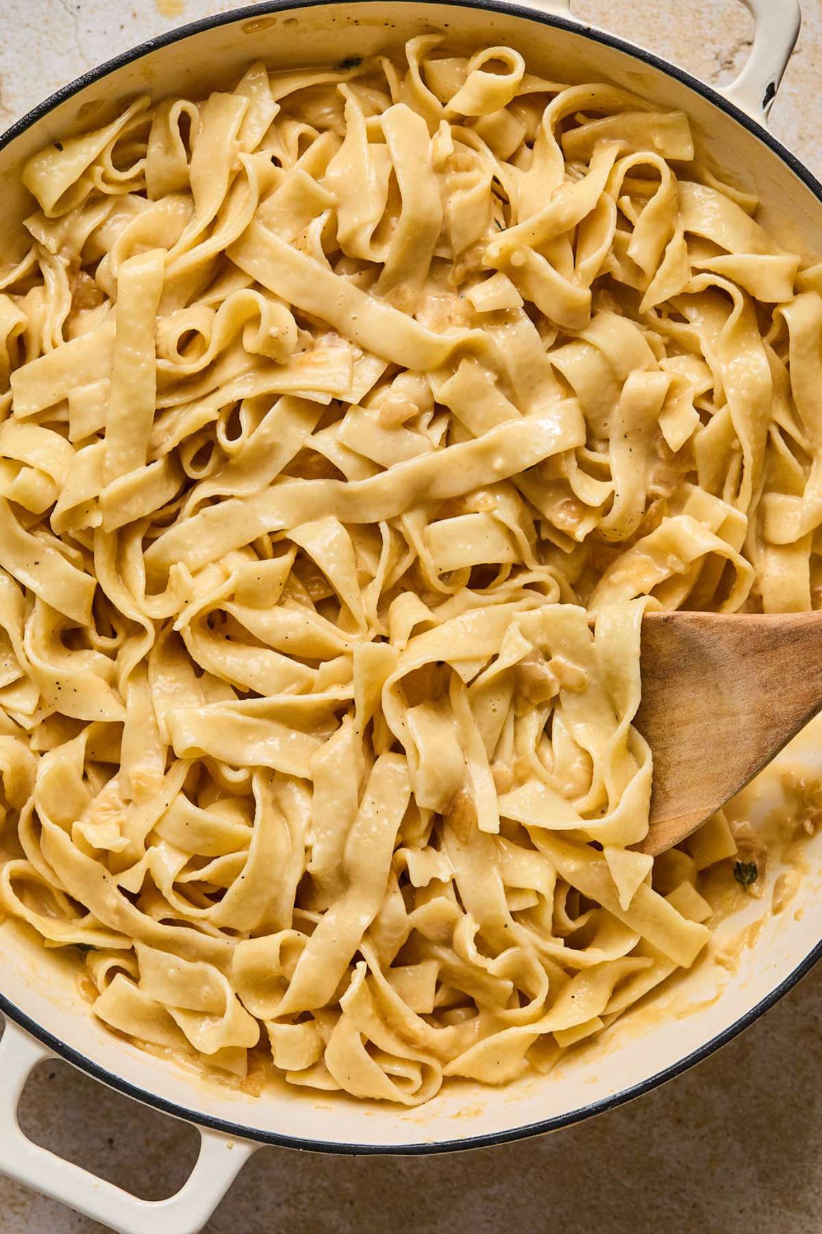 French onion pasta in a skillet with a wooden spoon resting to the side.