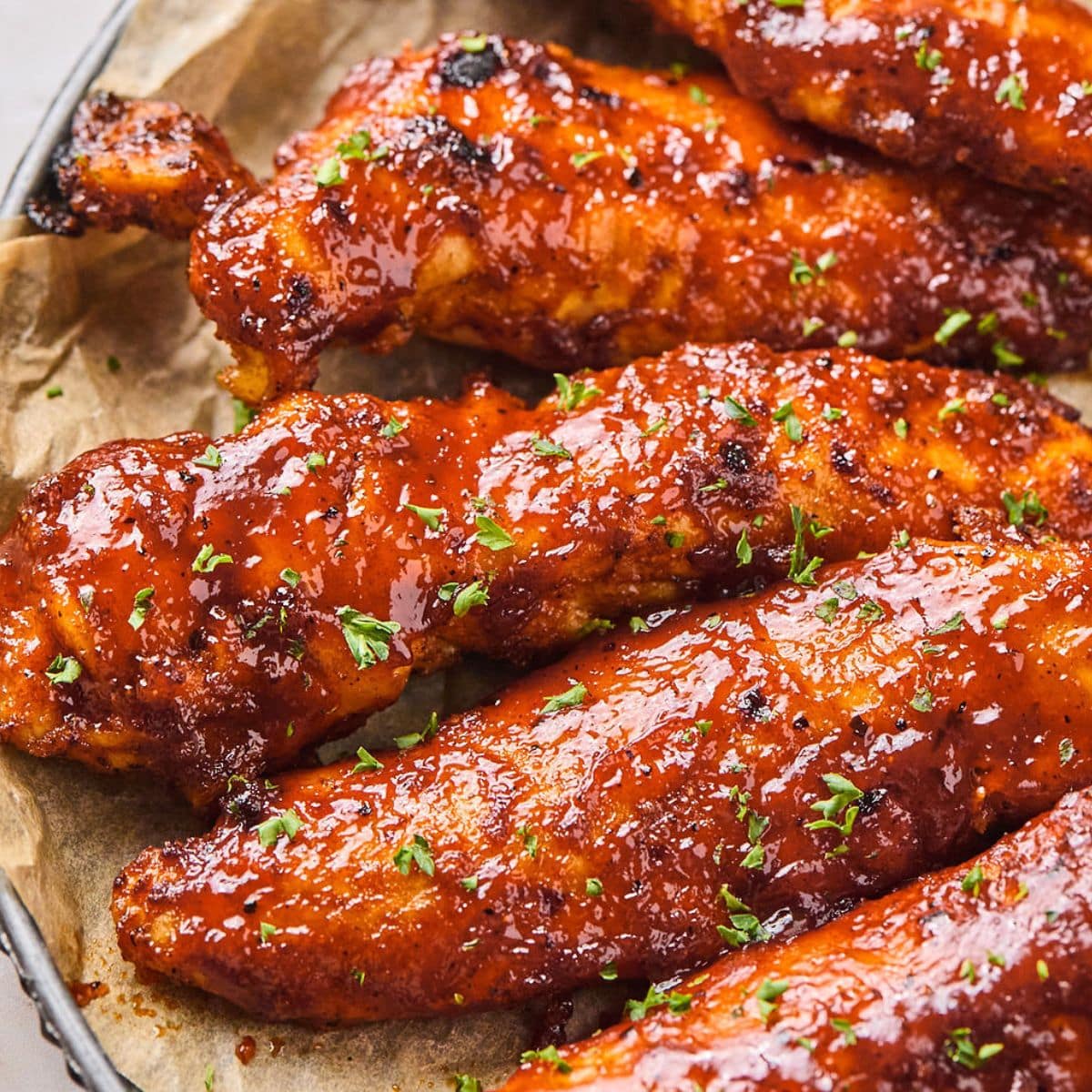 Close up of baked BBQ chicken tenders garnished with parsley.