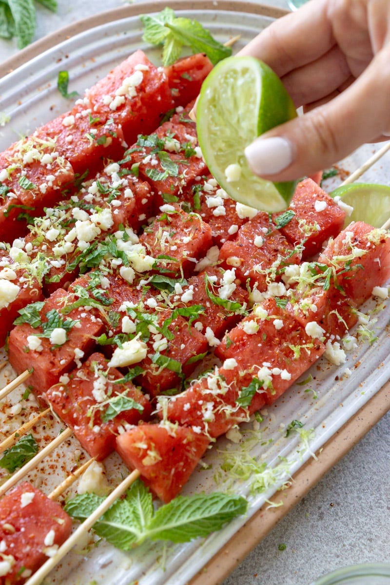 Lime being squeezed over watermelon Tajin skewers.