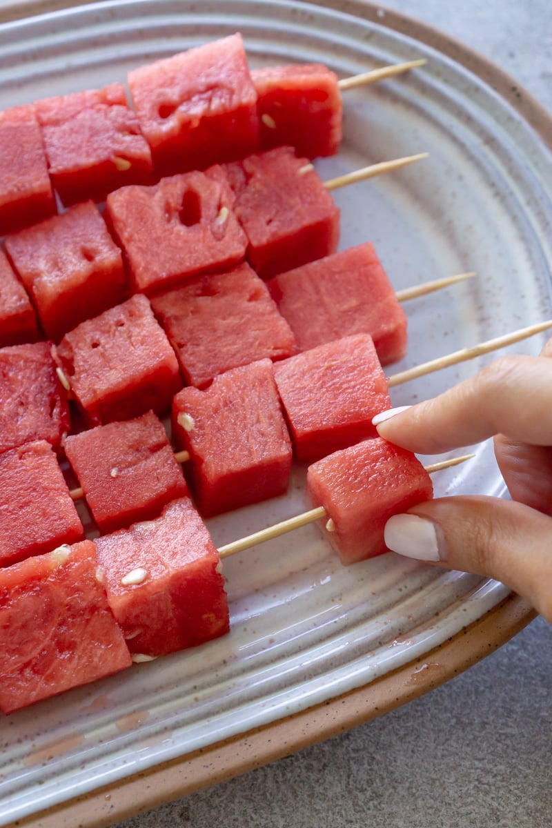 Watermelon cubes being threaded onto skewers.