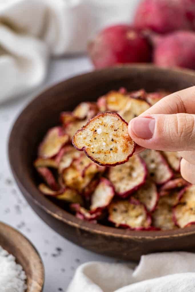 A hand holding a radish chip.