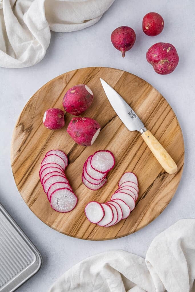 Thinly sliced radishes on a wood cutting board with a pairing knife.