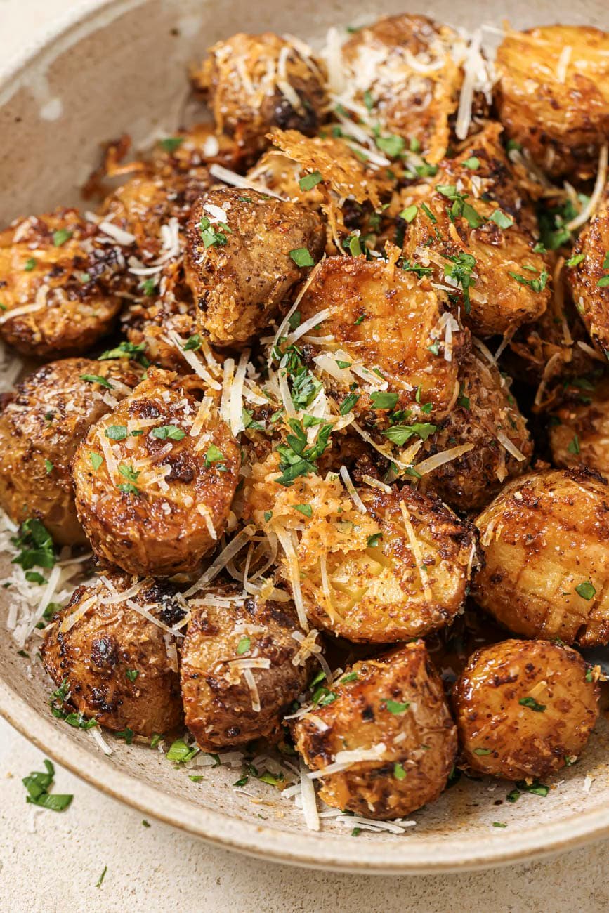 Halved potatoes, cooked, in a bowl, topped with parmesan cheese and parsley.