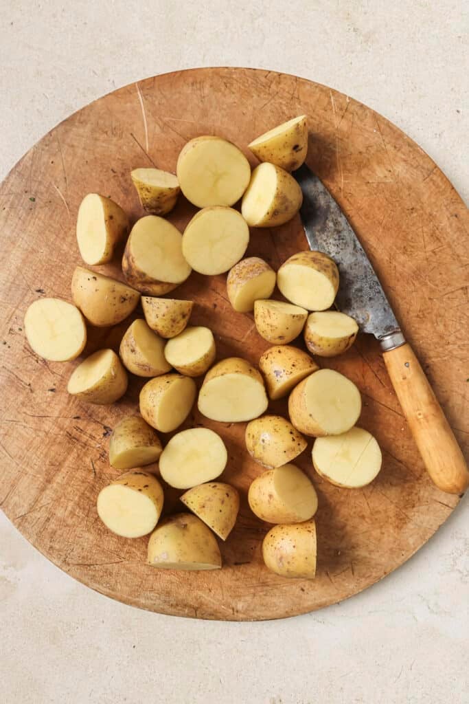 A bunch of potatoes halved, resting on top of a round cutting board, and a knife next to them.