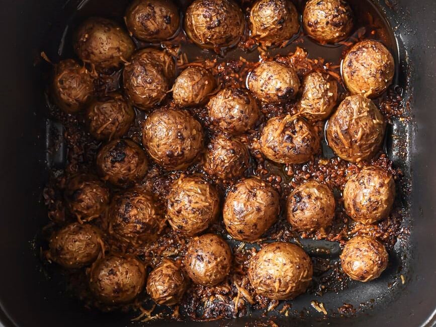 Halved potatoes face down in a black air fryer cooking basket.