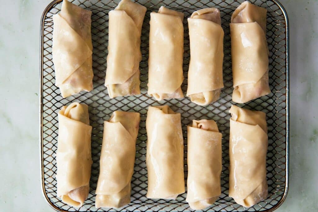 Uncooked egg rolls in an air fryer basket.