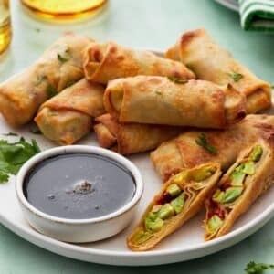 Egg rolls on a serving plate with dipping sauce.