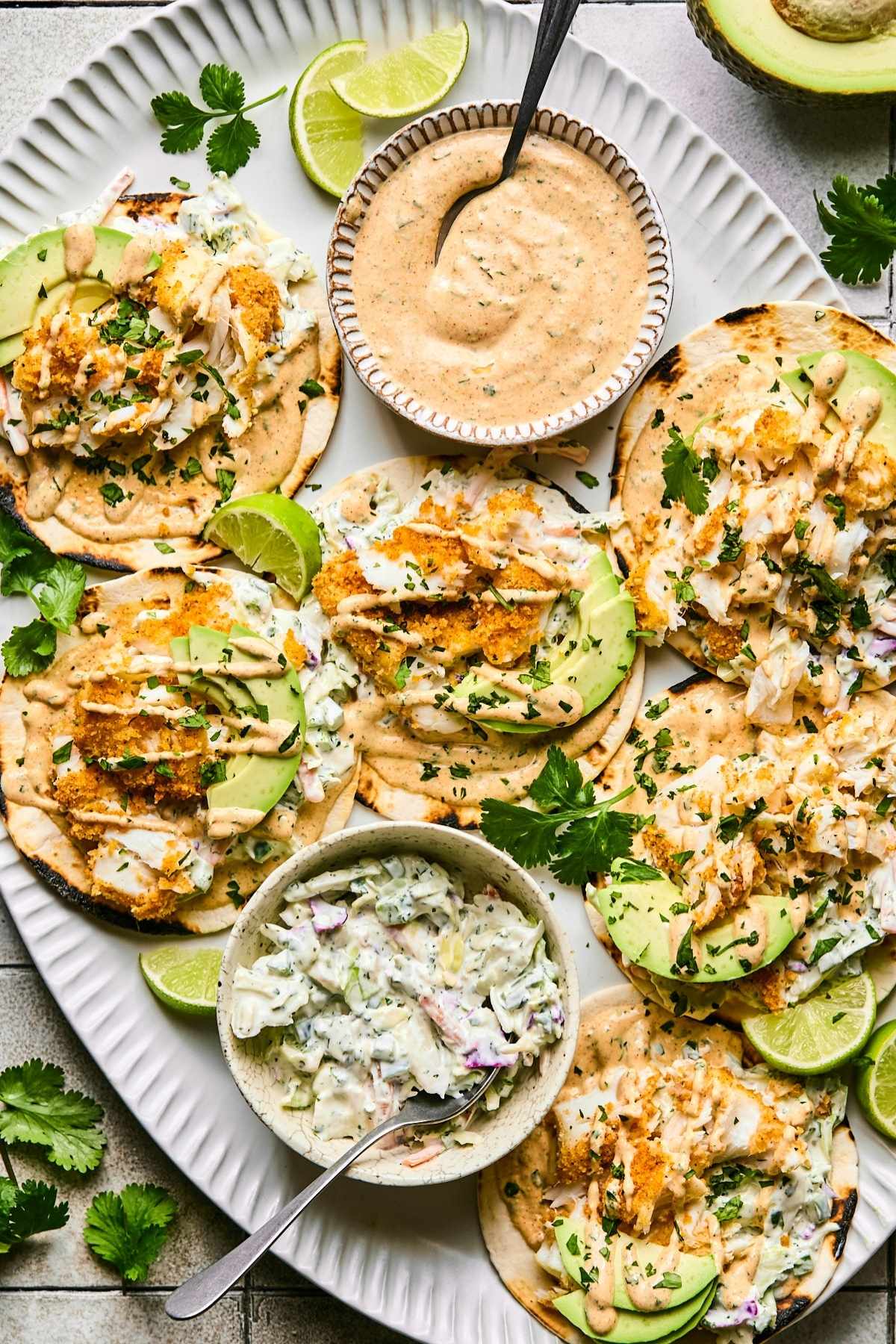 A platter of air fryer fish tacos with bowls of sauce and toppings on the side.