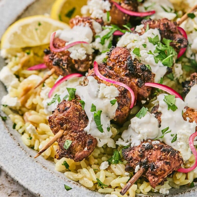 air fryer chicken skewers on a plat with slice red onions, a lemon slice, and parsley
