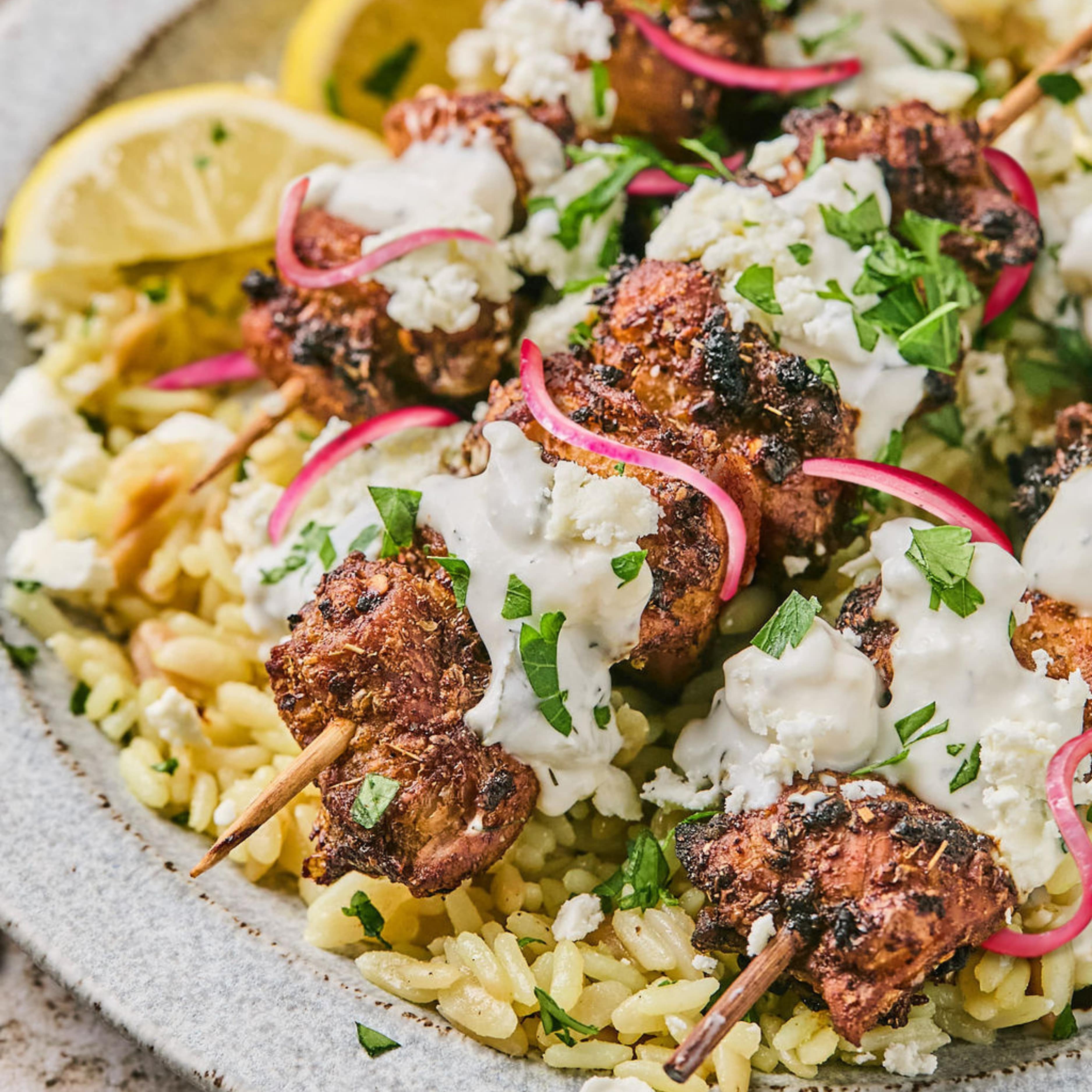 air fryer chicken skewers on a plat with slice red onions, a lemon slice, and parsley