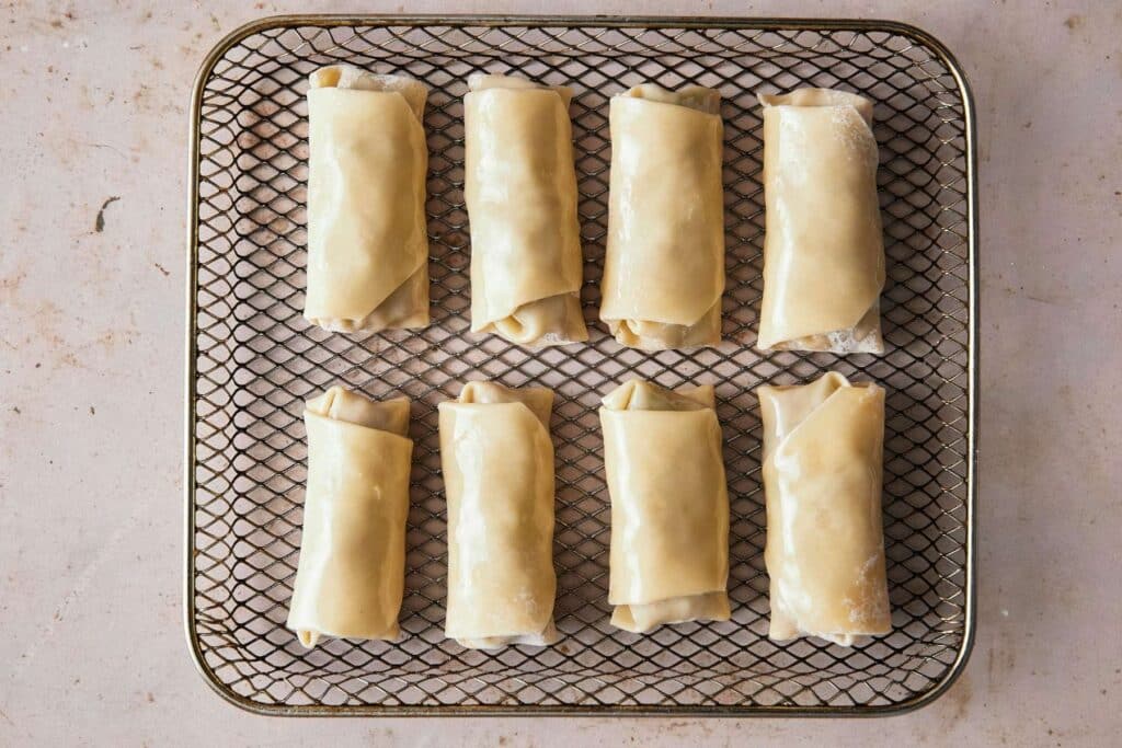 Egg rolls in an air fryer basket.