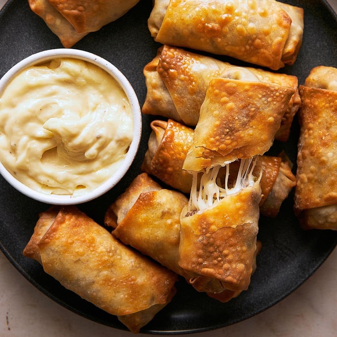 A plate of philly cheesesteak egg rolls with garlic aioli.