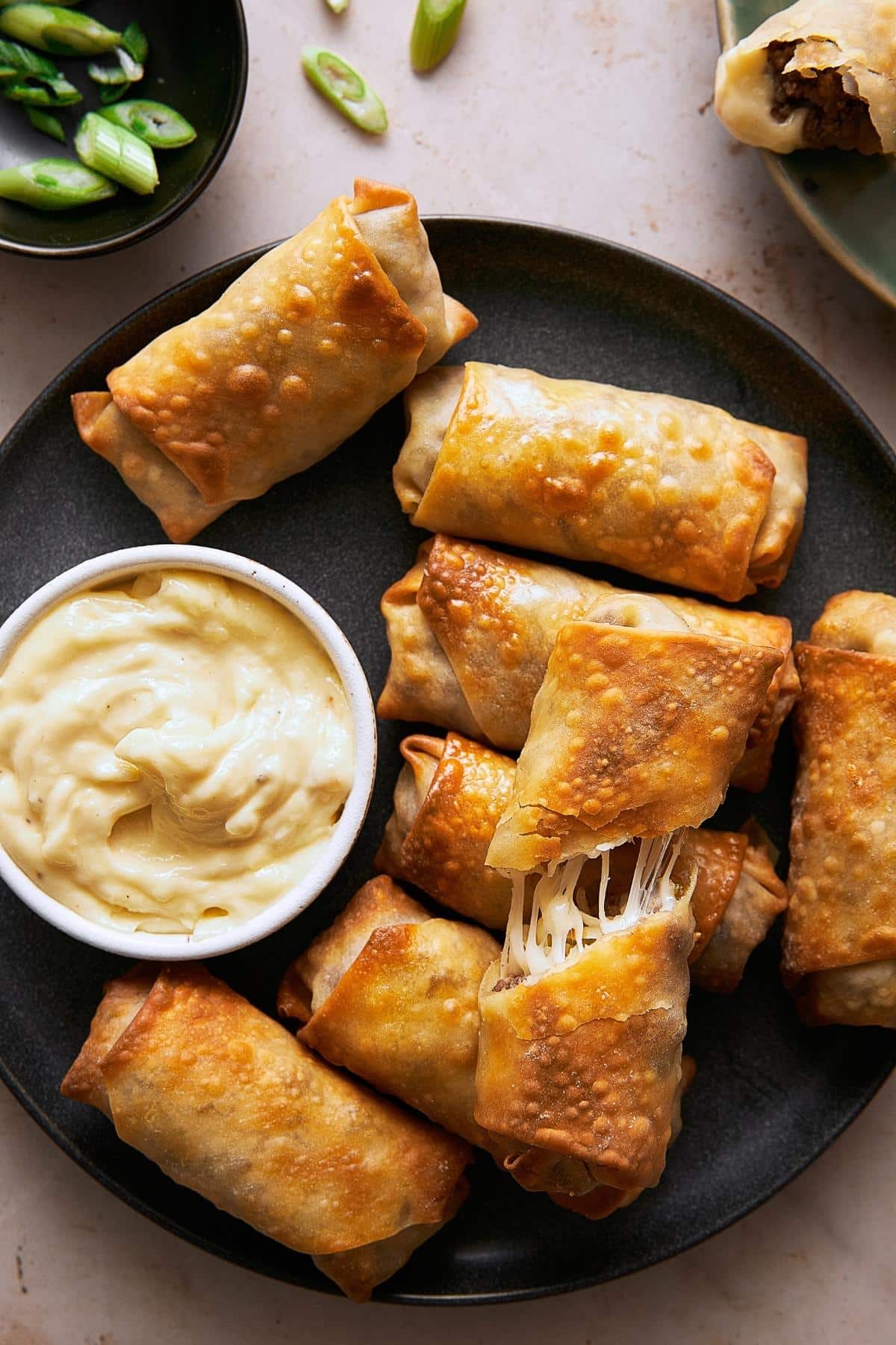 A plate of golden brown cheesesteak egg rolls with a dish of garlic aioli.
