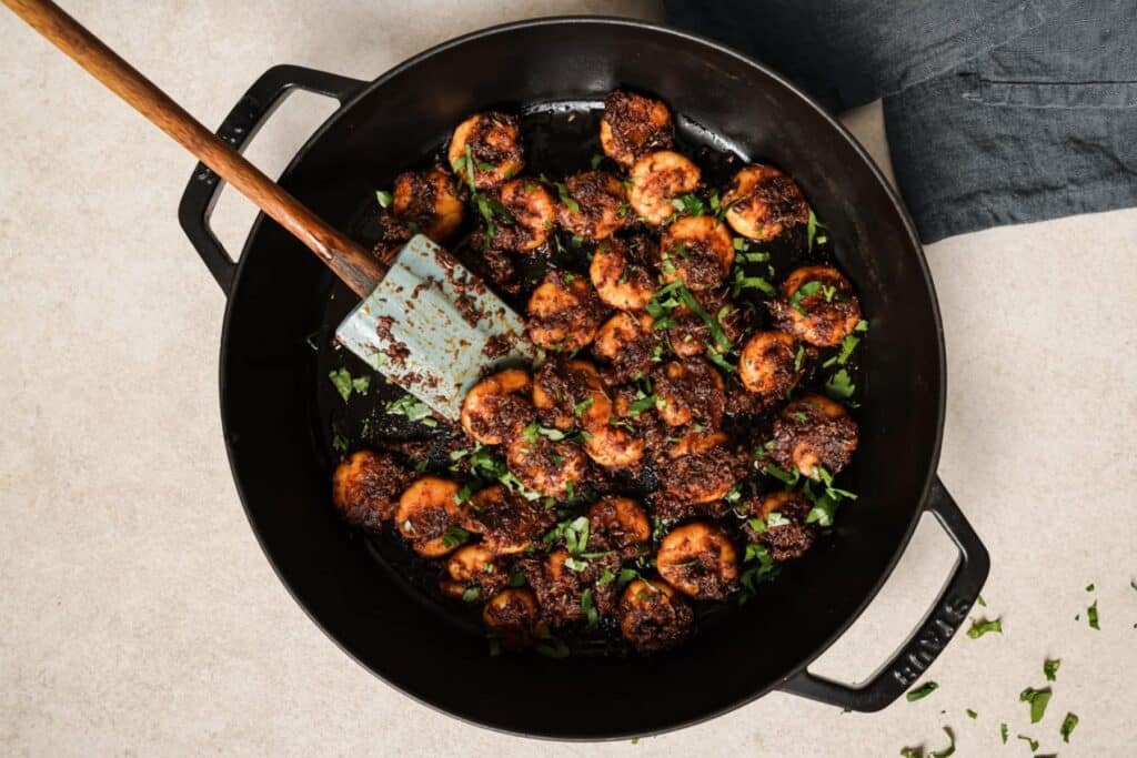Adding garnish to shrimp in a skillet.