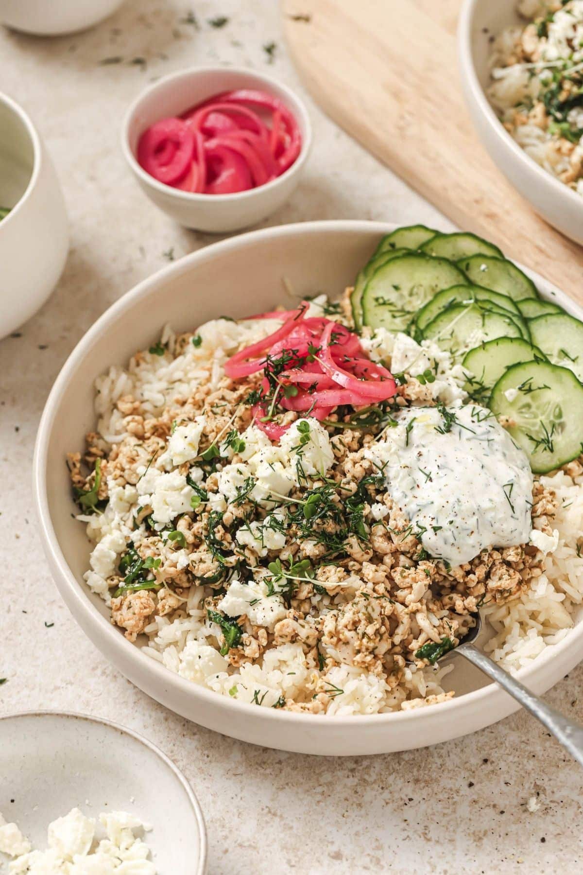 A greek chicken and rice bowl with smaller dishes of toppings on the table.