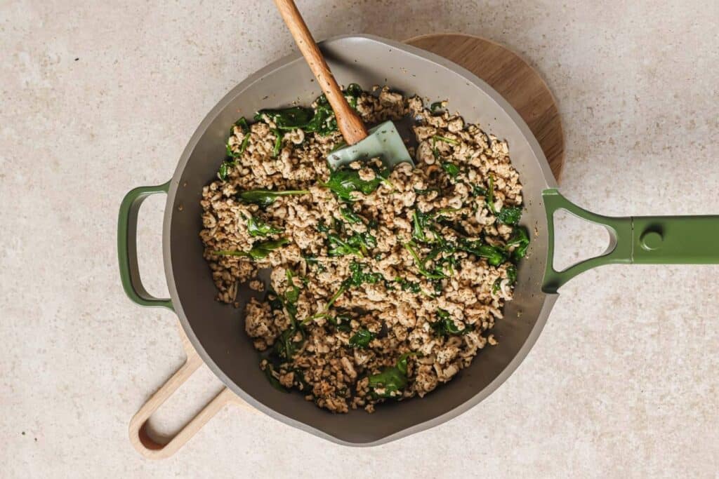 Mixing spinach into browned chicken.