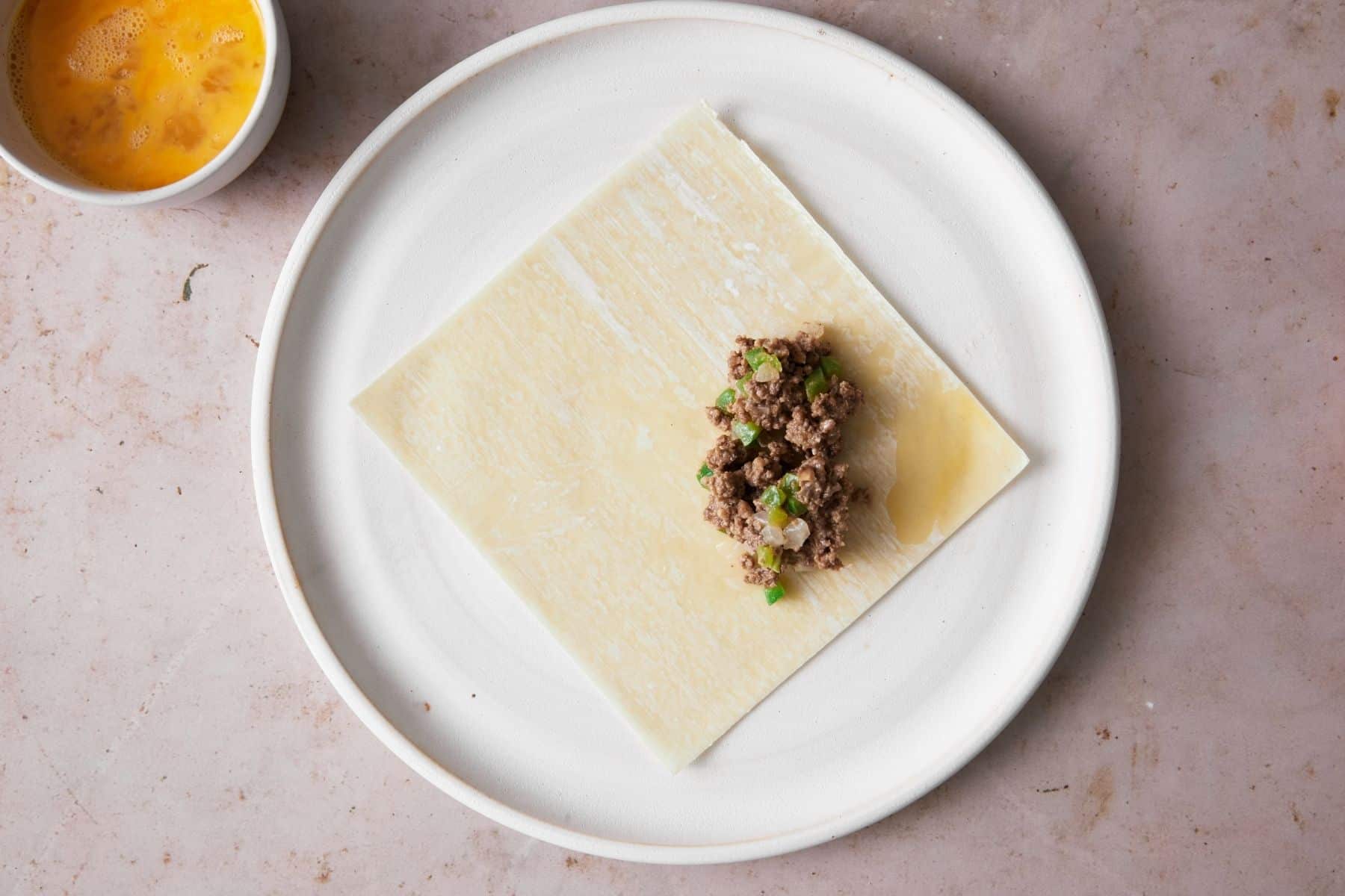 A scoop of filling on an egg roll wrapper.