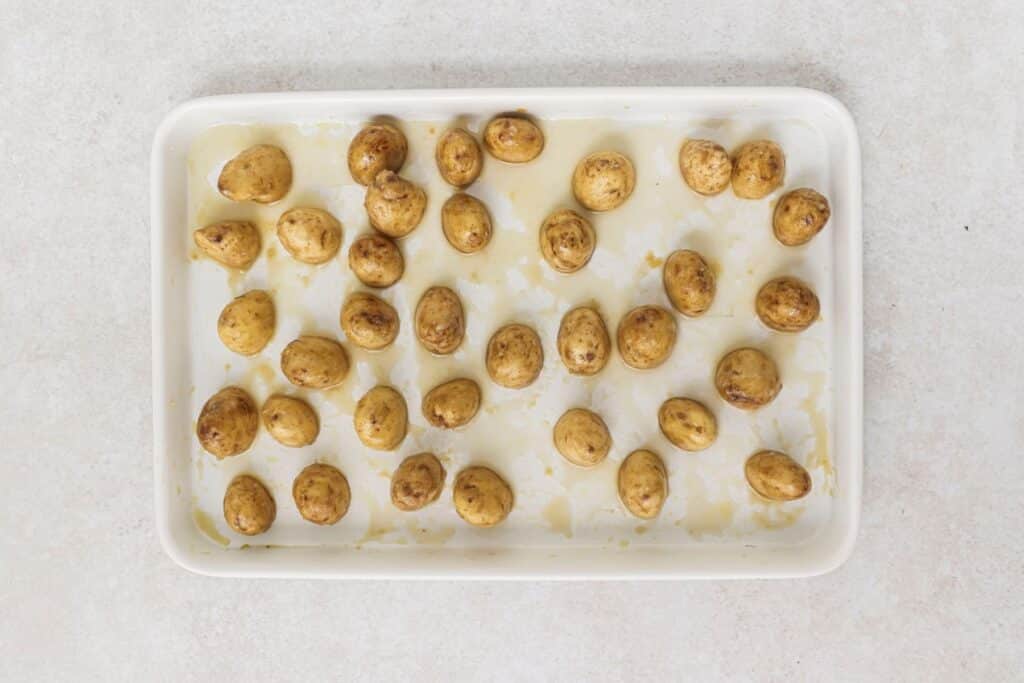 Seasoned potatoes cut side down on a baking sheet.