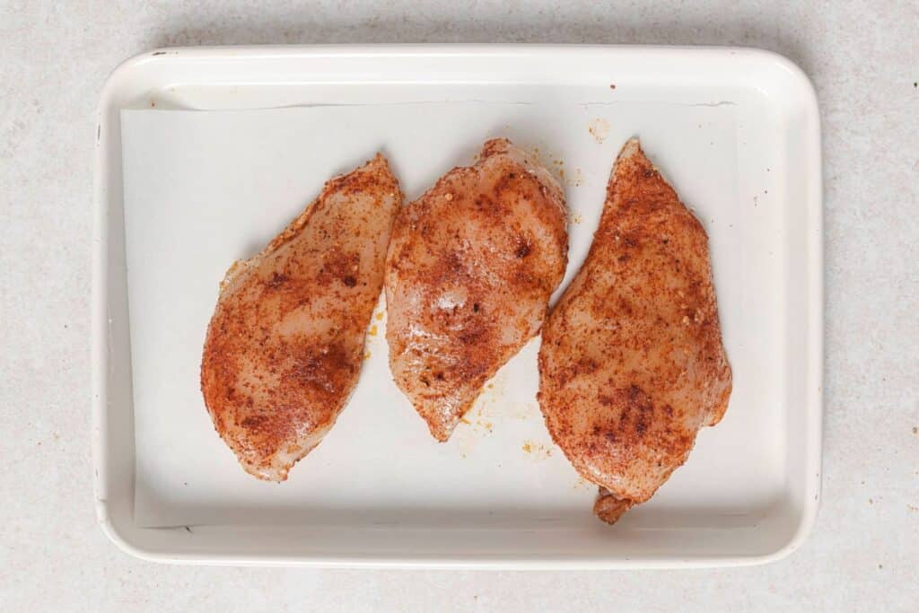 Seasoned chicken breasts on a baking sheet.