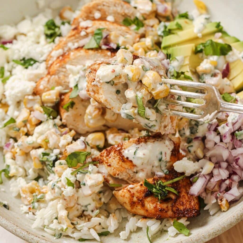 A fork picking up a bite of street corn chicken and rice.