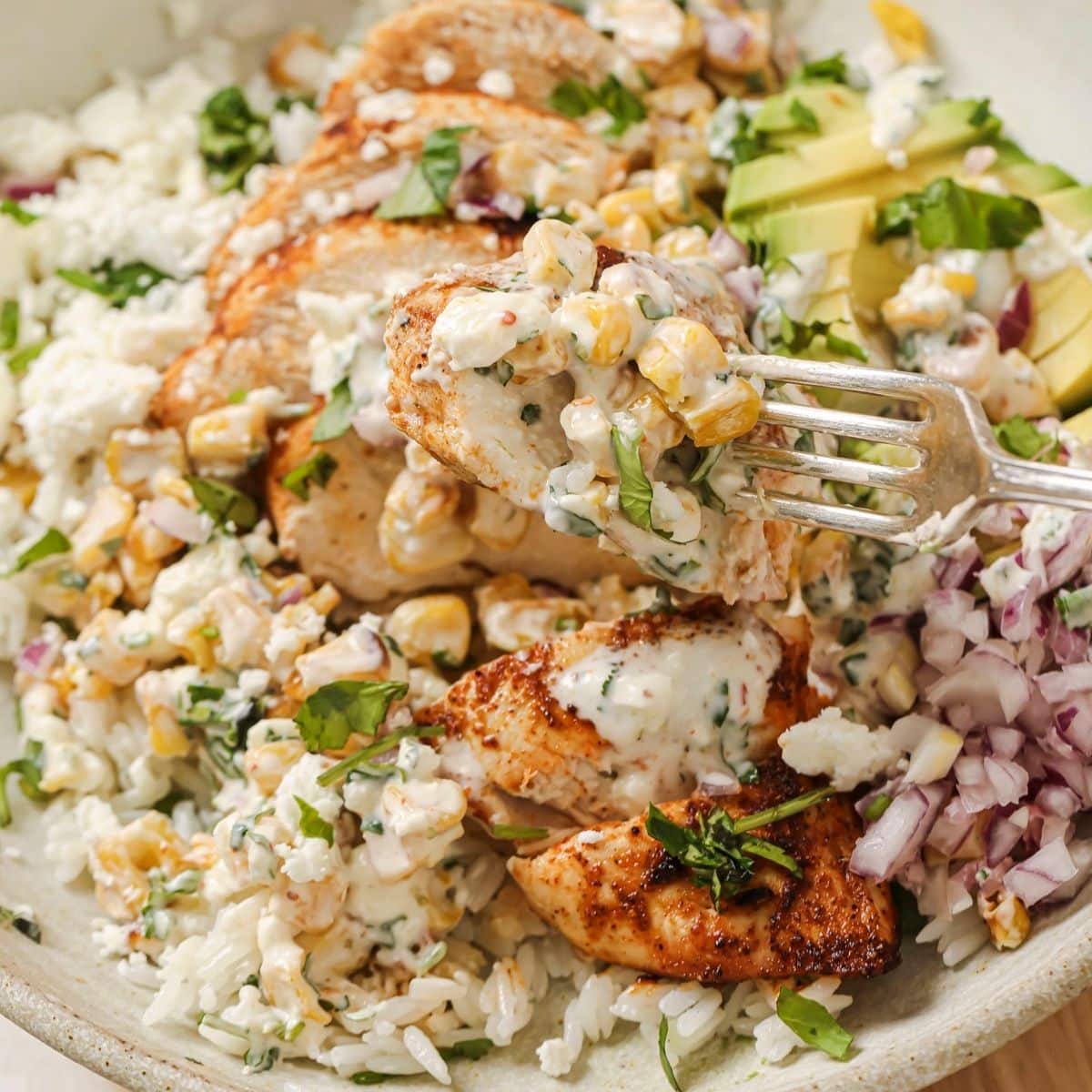 A fork picking up a bite of street corn chicken and rice.
