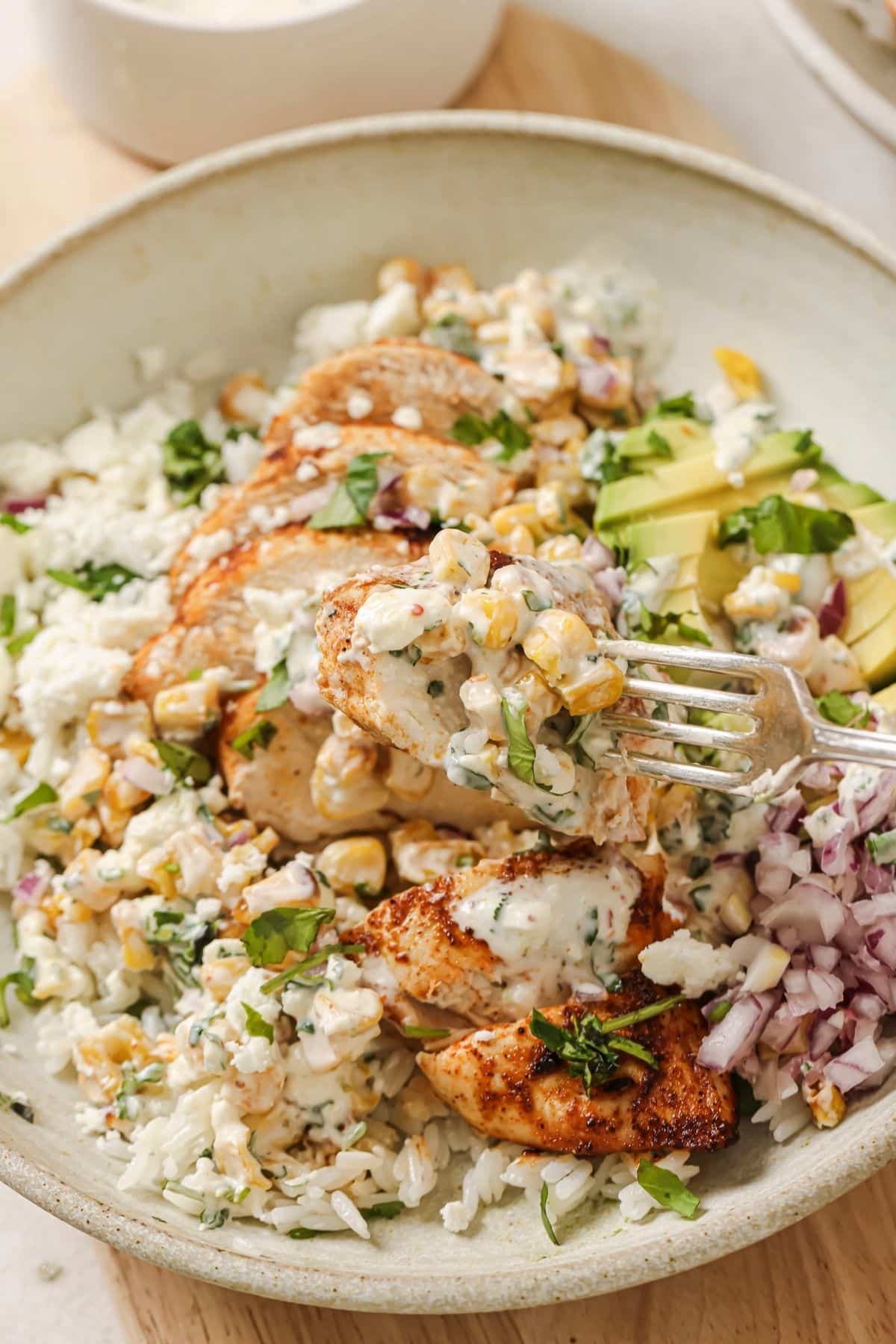 Close up shot of a fork picking up a bite of street corn chicken and rice.