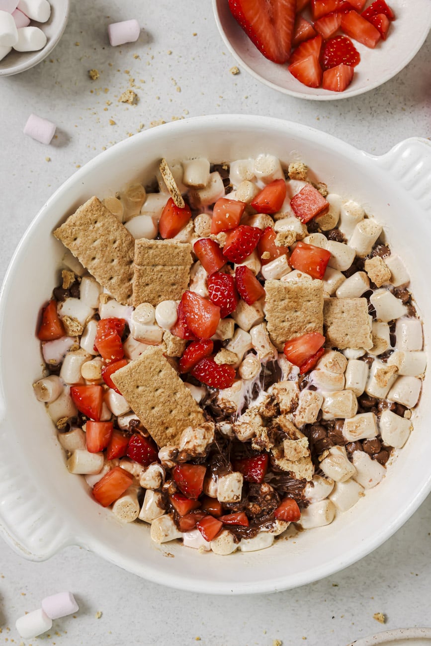 There are cut up strawberries, melted mini marshmallows and chocolate, and graham cracker pieces in a bowl.