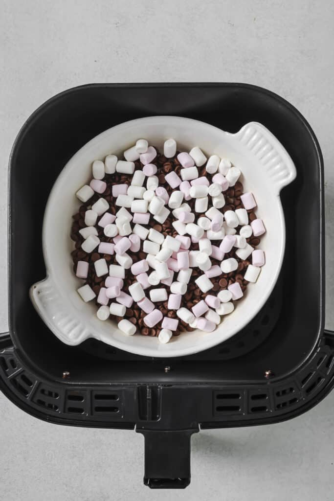 White baking dish with mini marshmallows and chocolate sitting in an air fryer basket