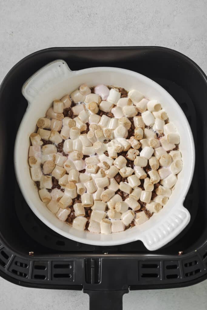 White baking dish with melted marshmallows and chocolate sitting in an air fryer basket.
